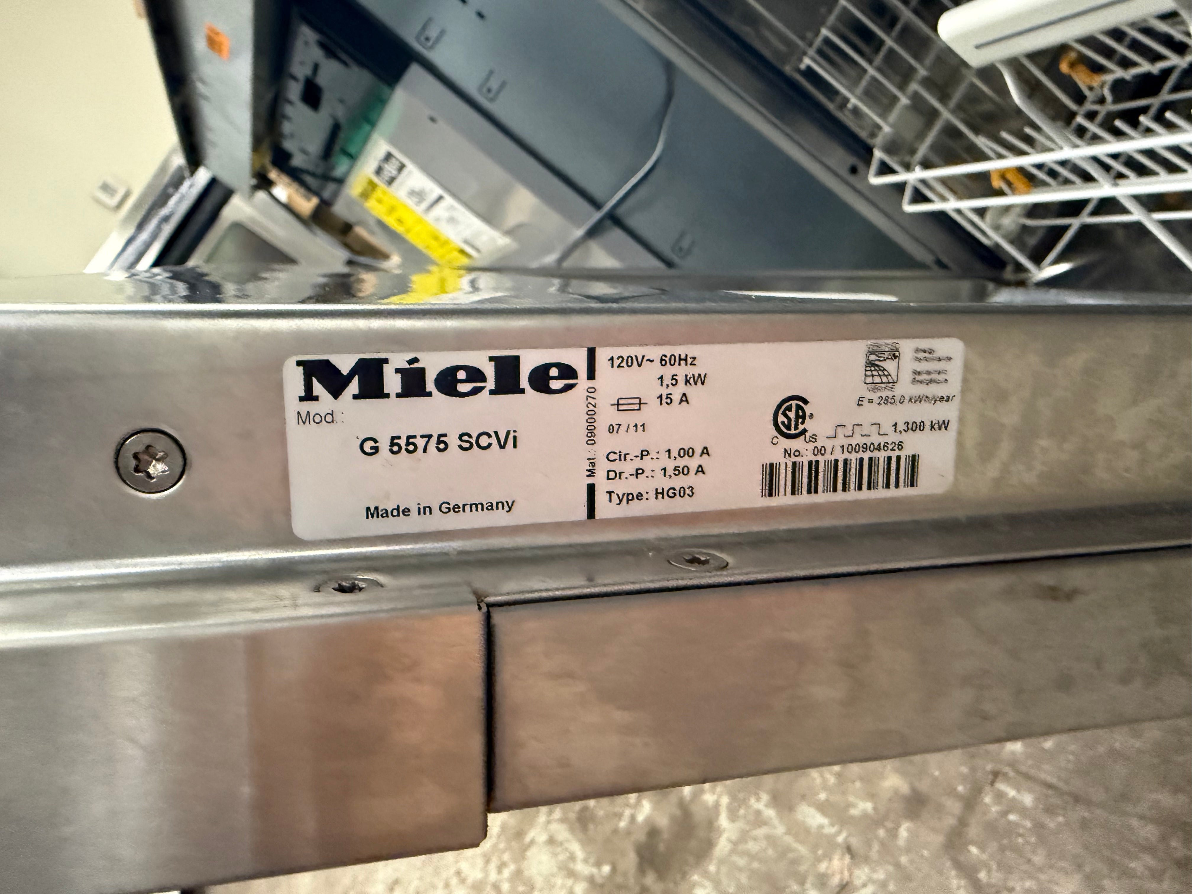 A close-up of a stainless steel dishwasher showing a white Miele product label with model details G 5575 SCVI.