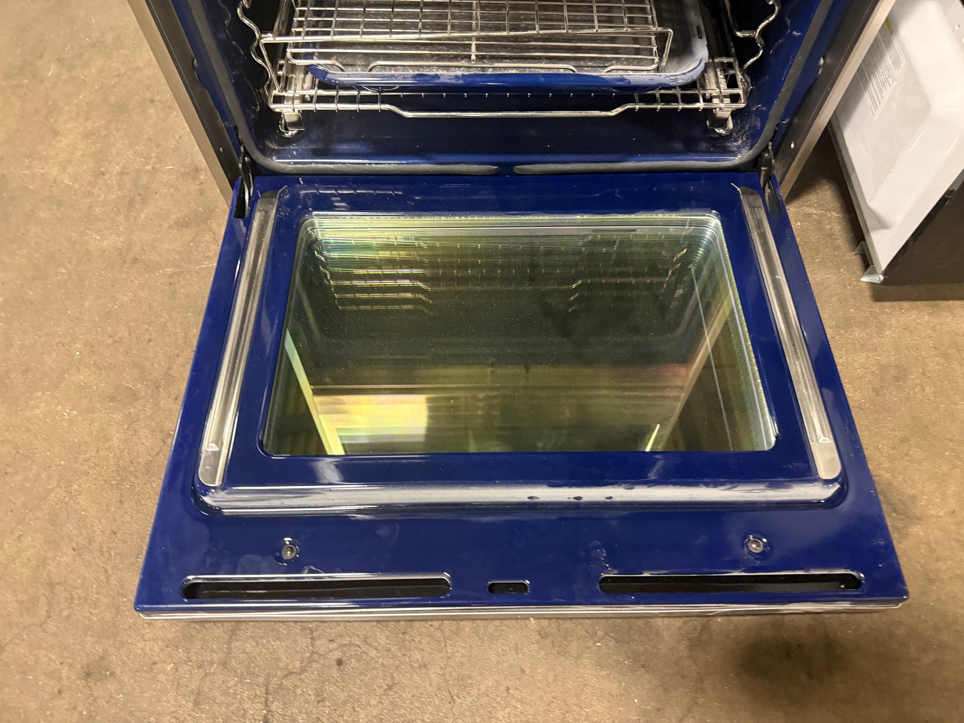 A blue oven with its door open, showing the interior racks and glass door, photographed on a concrete floor.