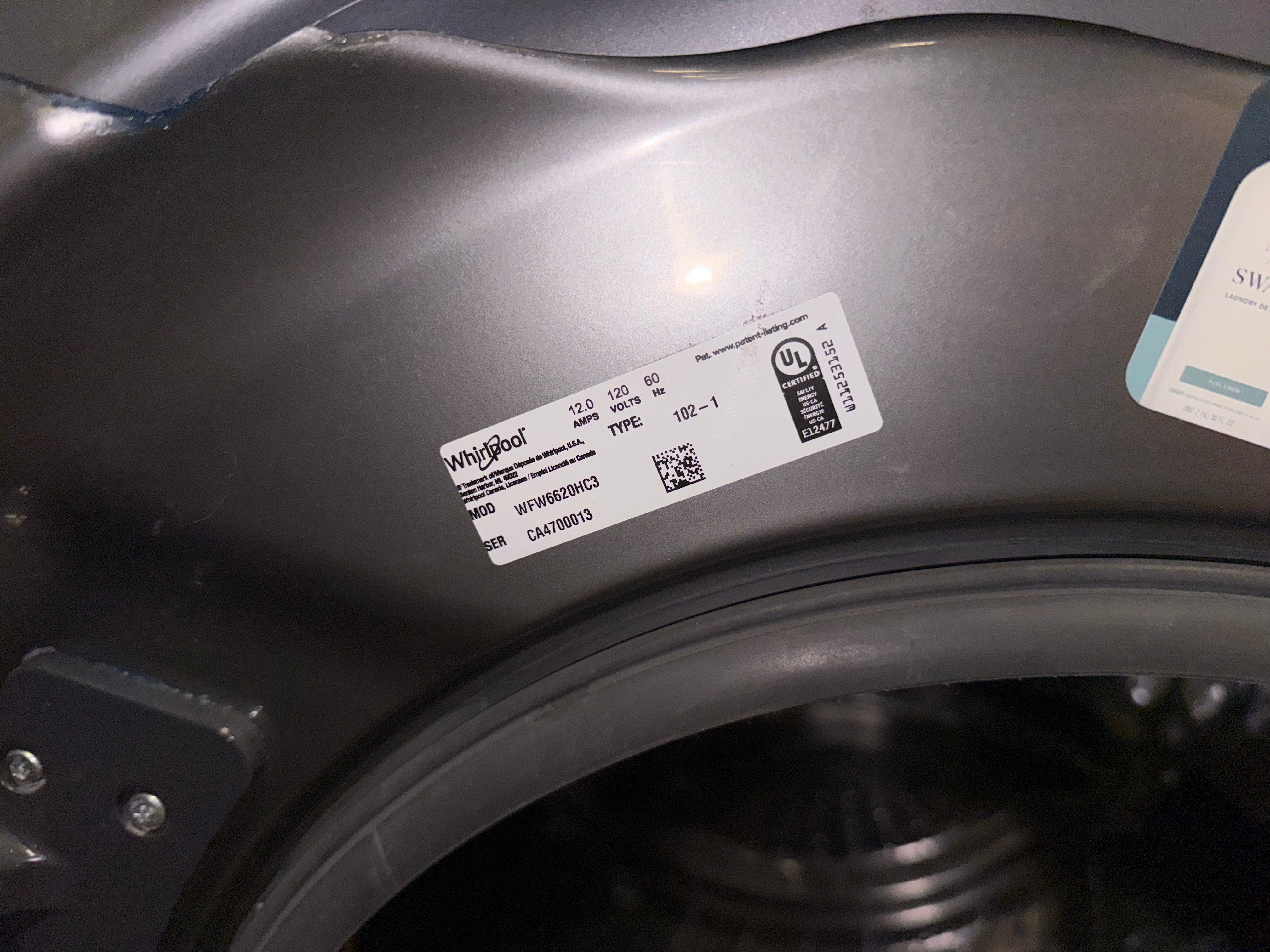 A close-up of a dark gray appliance interior, likely a washing machine drum opening, showing a white Whirlpool product label and a partial second label.
