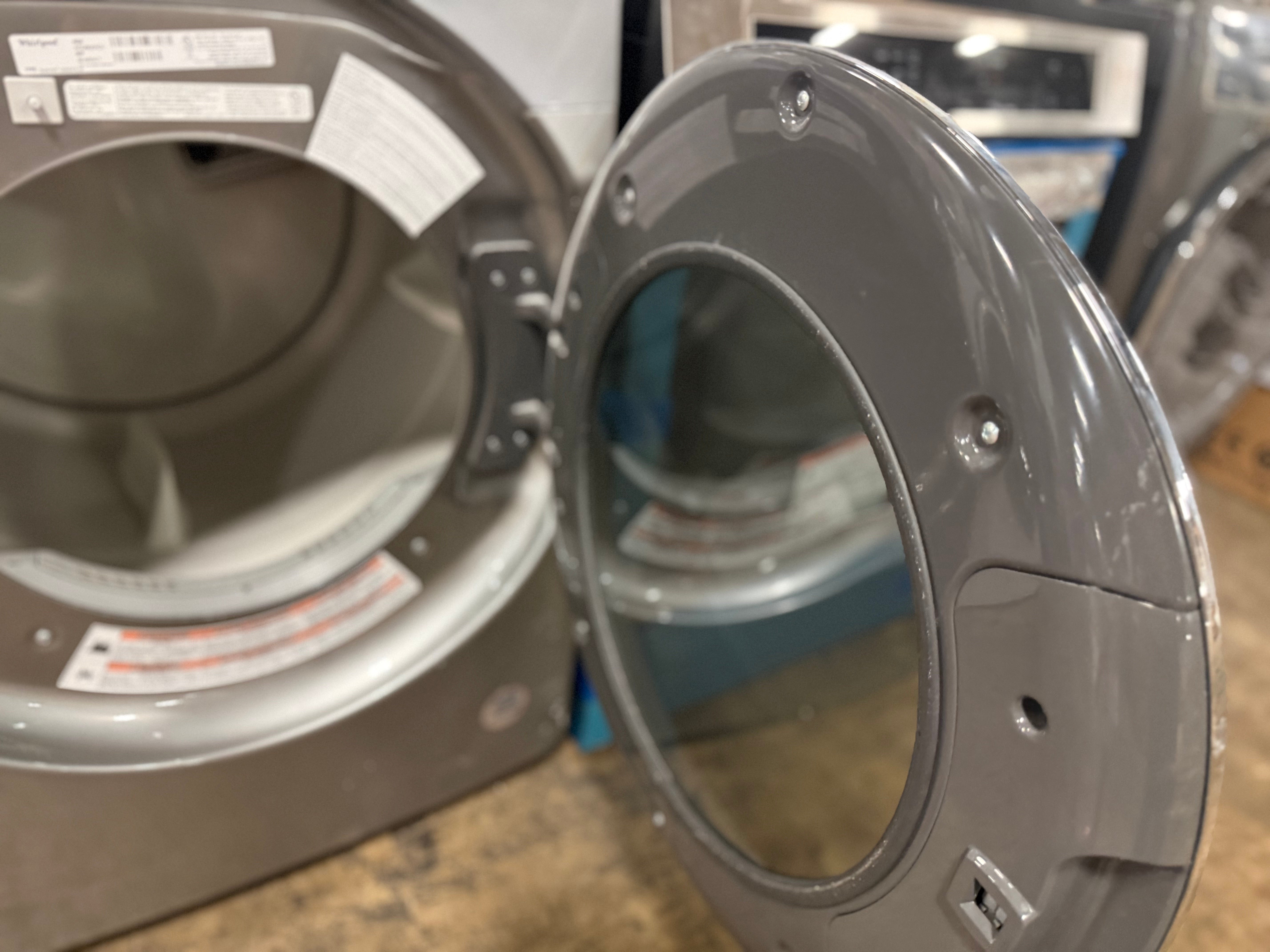 A close-up of a gray appliance door frame or panel standing open next to a similar appliance interior, photographed in a workshop or showroom setting.