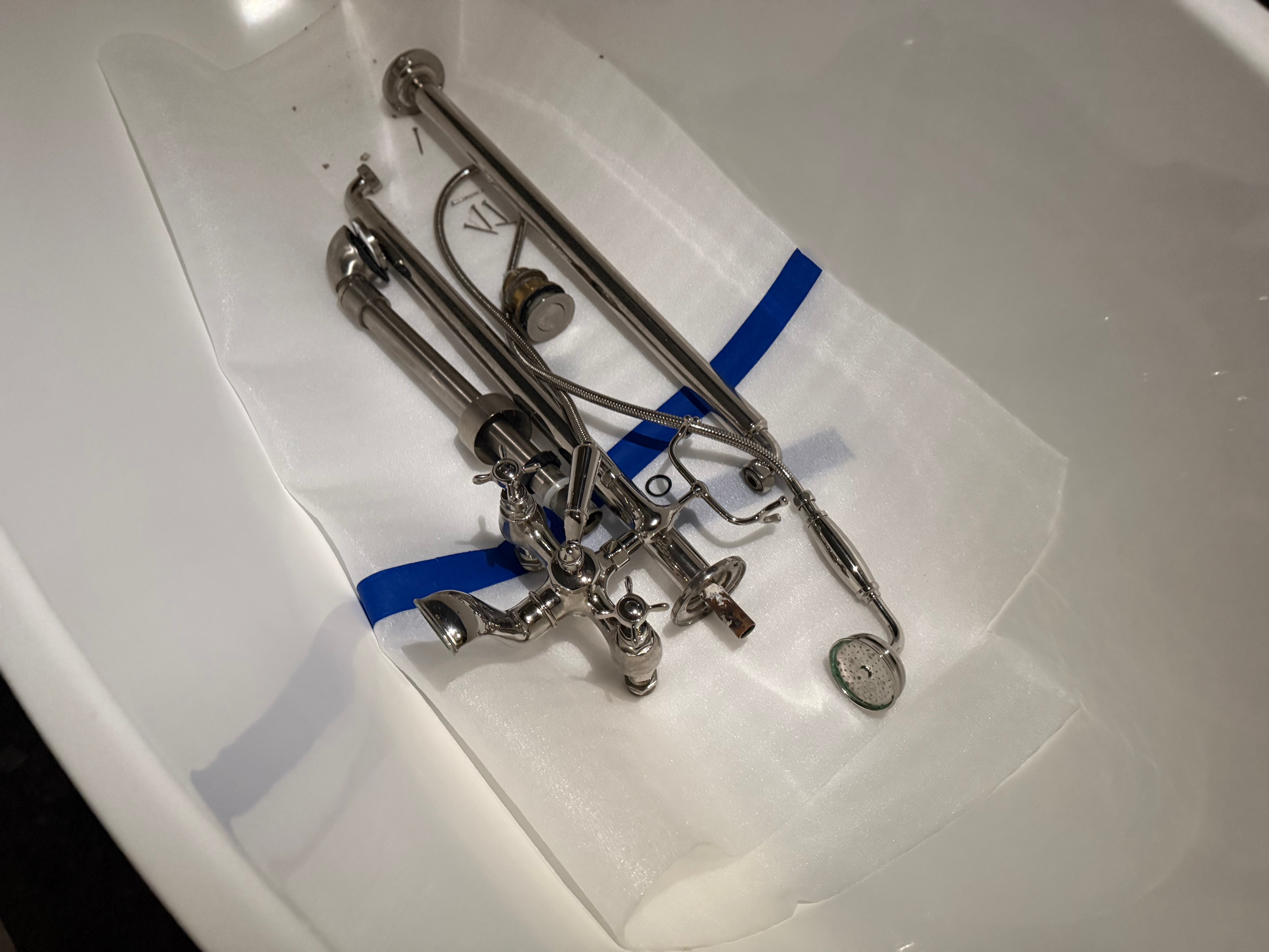 A set of polished silver metal faucet parts and fixtures laid out on a white protective sheet inside a white sink basin.