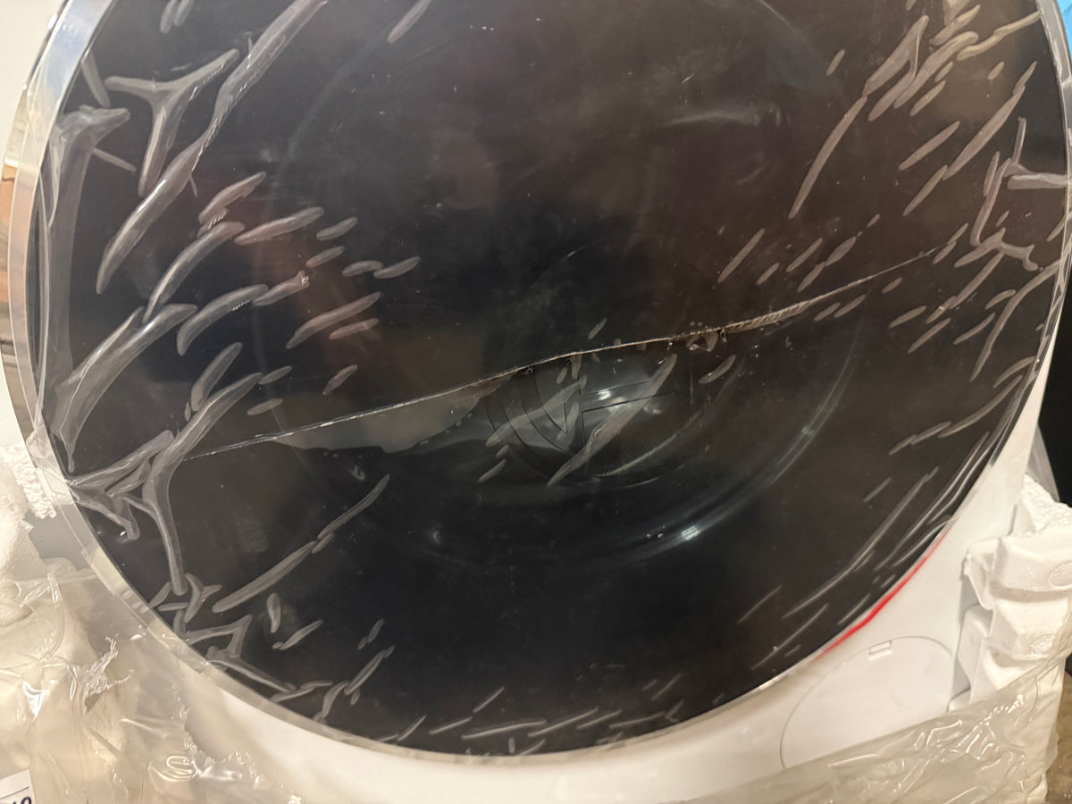 A close-up of a black circular appliance or container with a cracked transparent protective film on its outer surface, resting on a white base with some crumpled plastic visible.