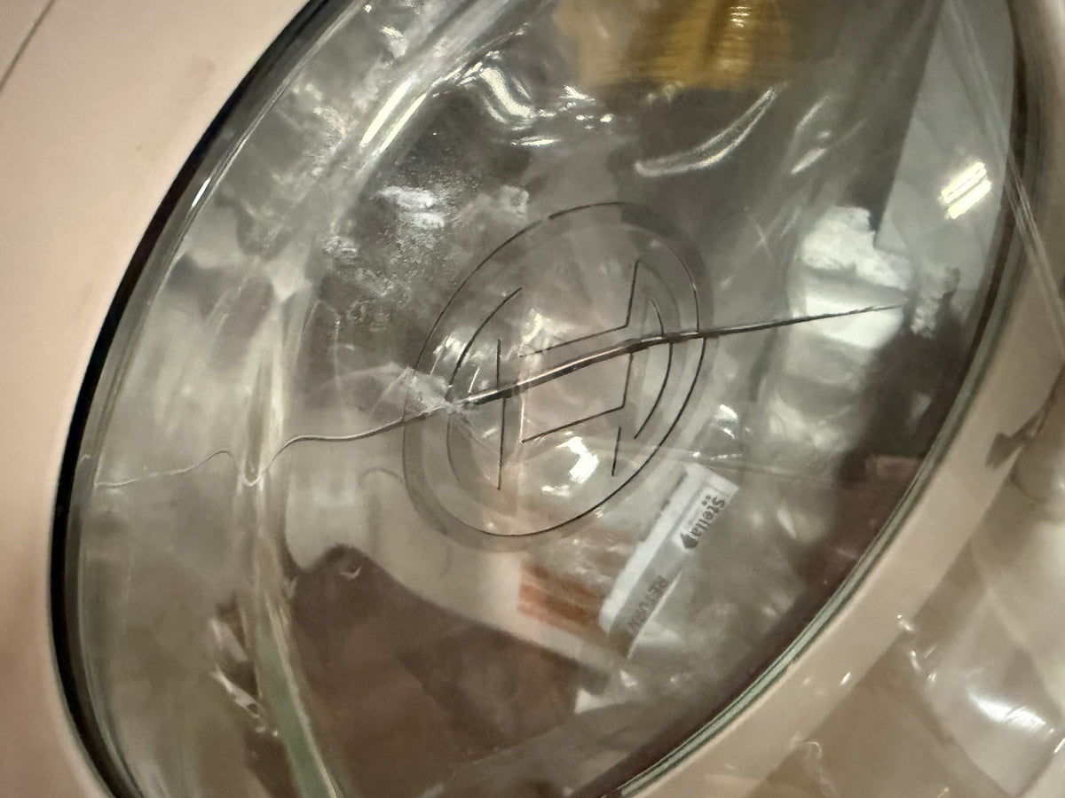 A close-up of a clear glass bowl with a cracked rim and a visible hairpin lodged inside, set against a beige appliance background.
