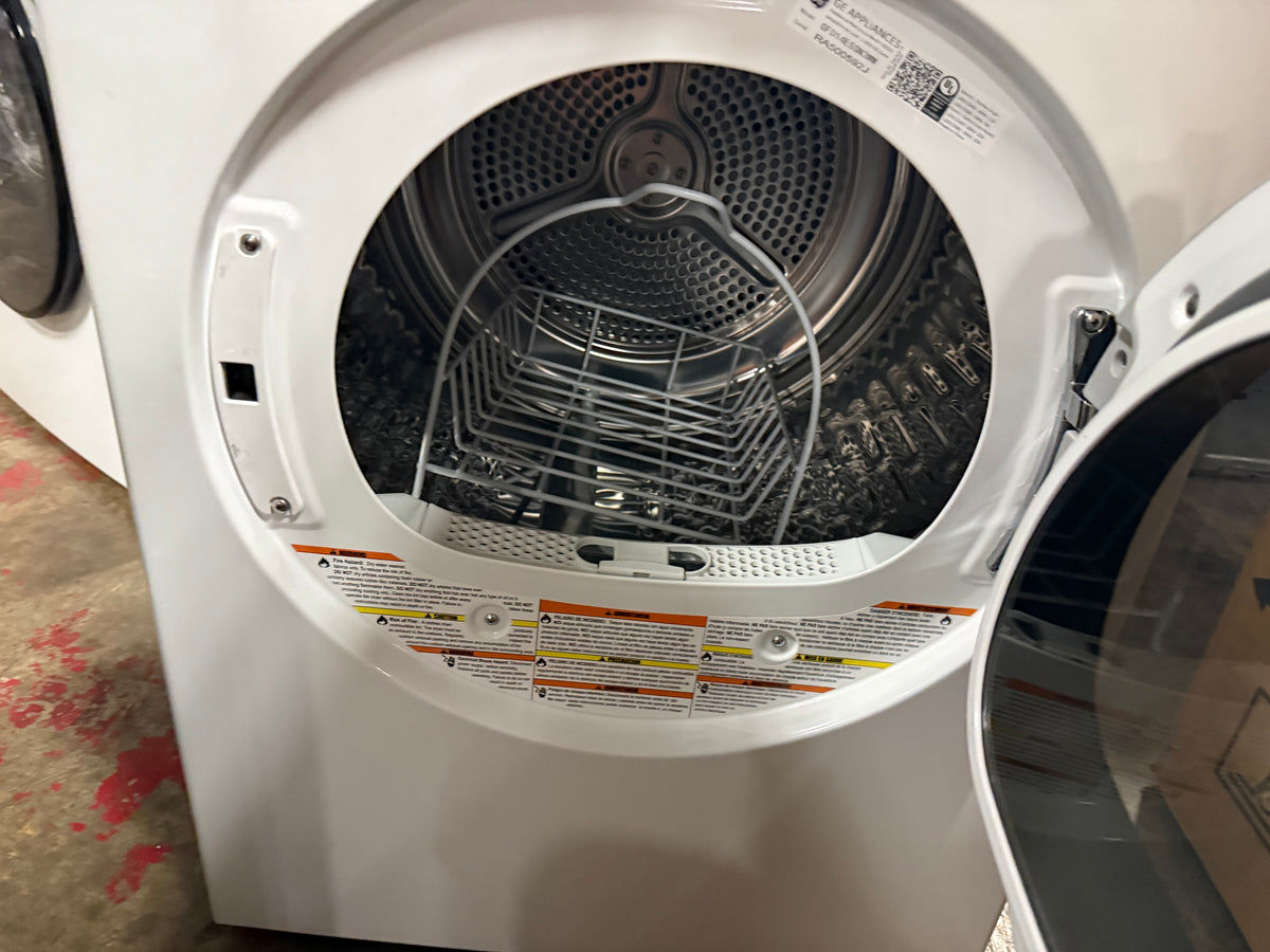 White front-load dryer with the door open, showing the stainless steel drum, inner basket, and warning labels inside the drum.