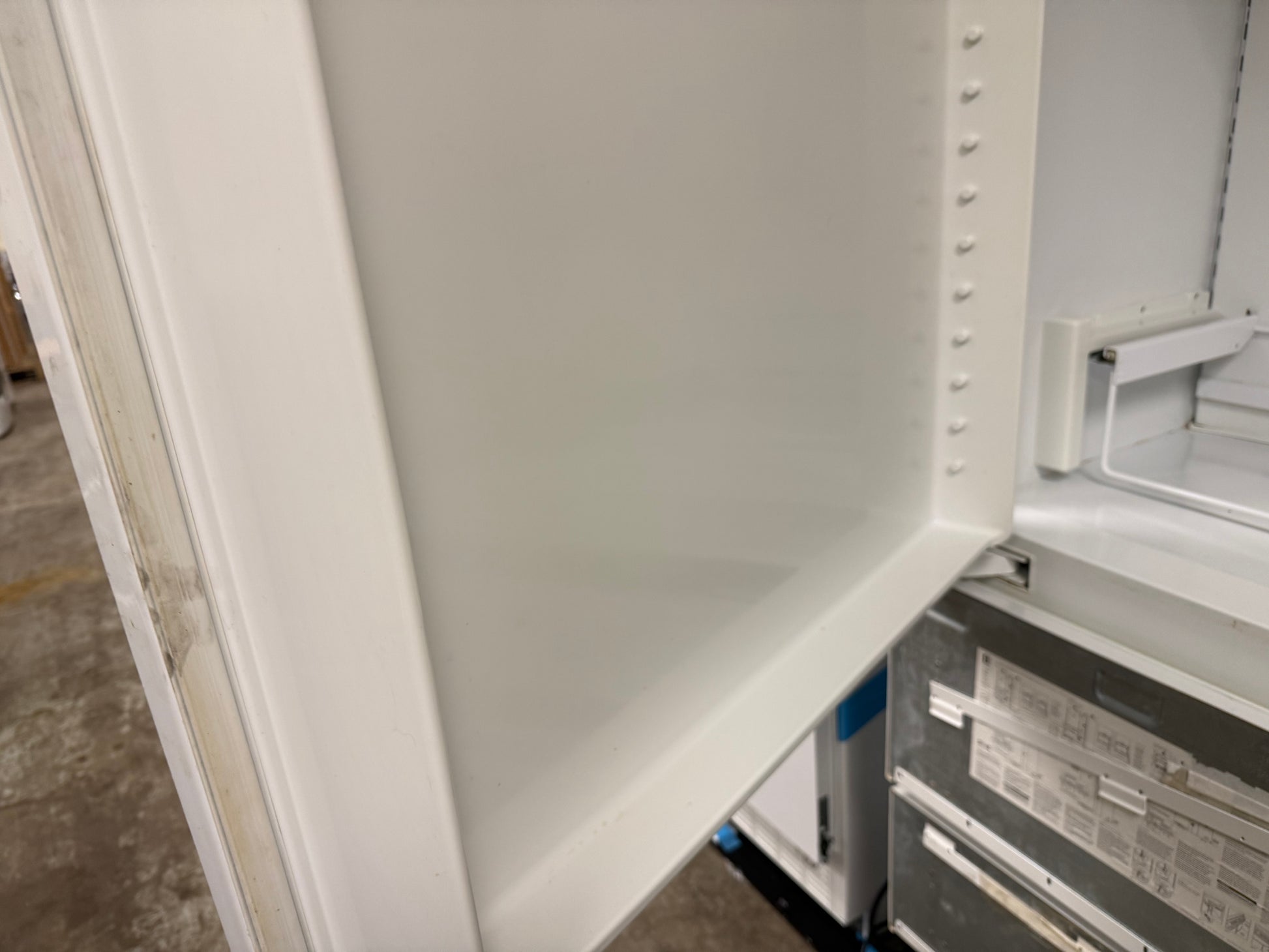 Close-up of the interior white door panel of a refrigerator, showing the inner frame and part of the lower shelf area.