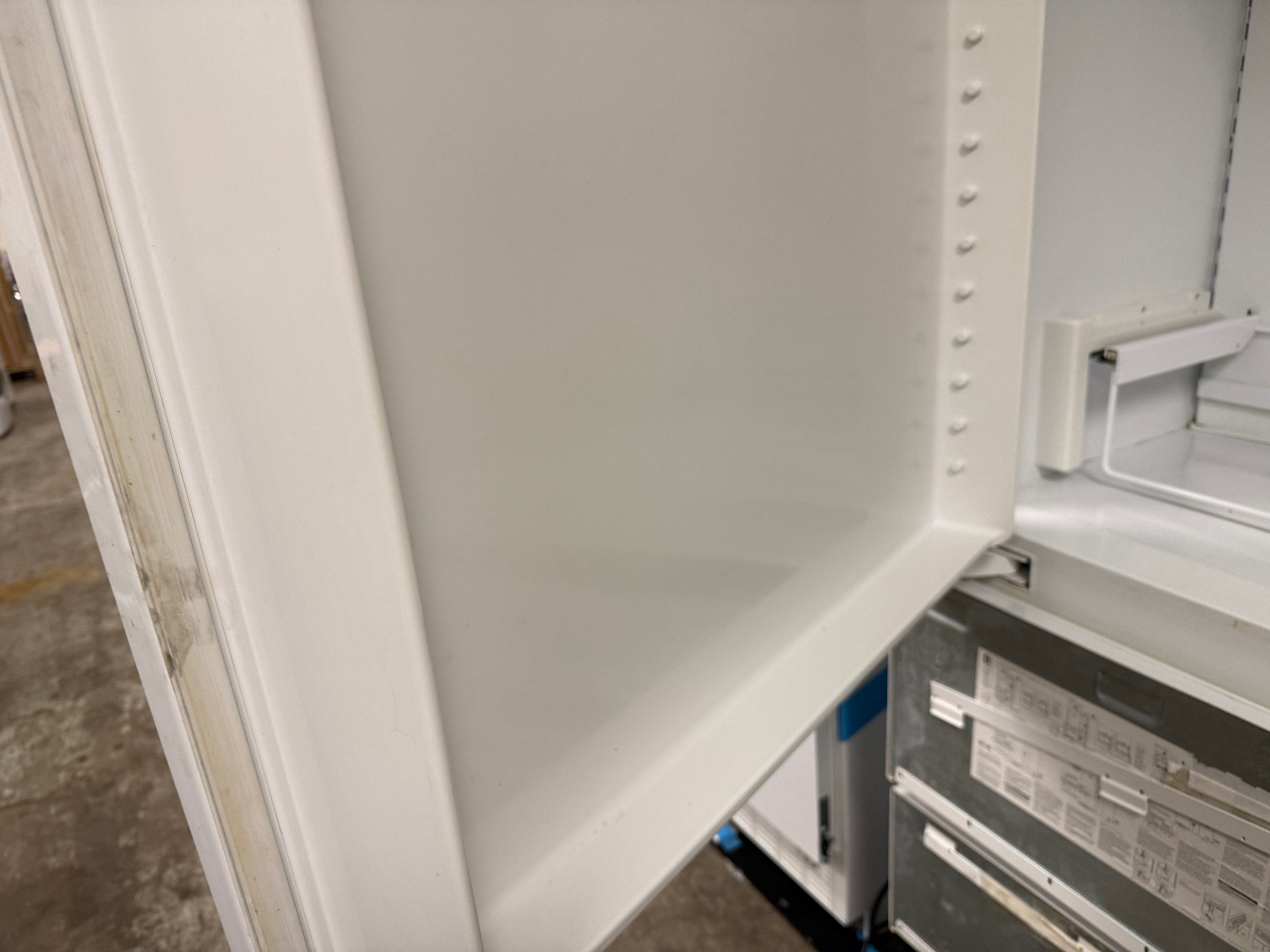 Close-up of the interior white door panel of a refrigerator, showing the inner frame and part of the lower shelf area.
