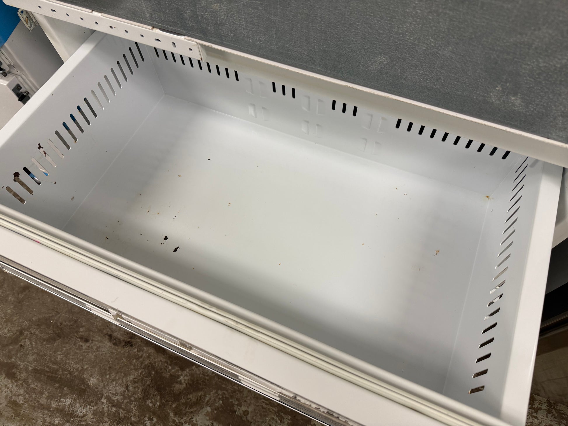A white plastic drawer organizer insert with ventilation slots, shown pulled out of a white drawer unit.