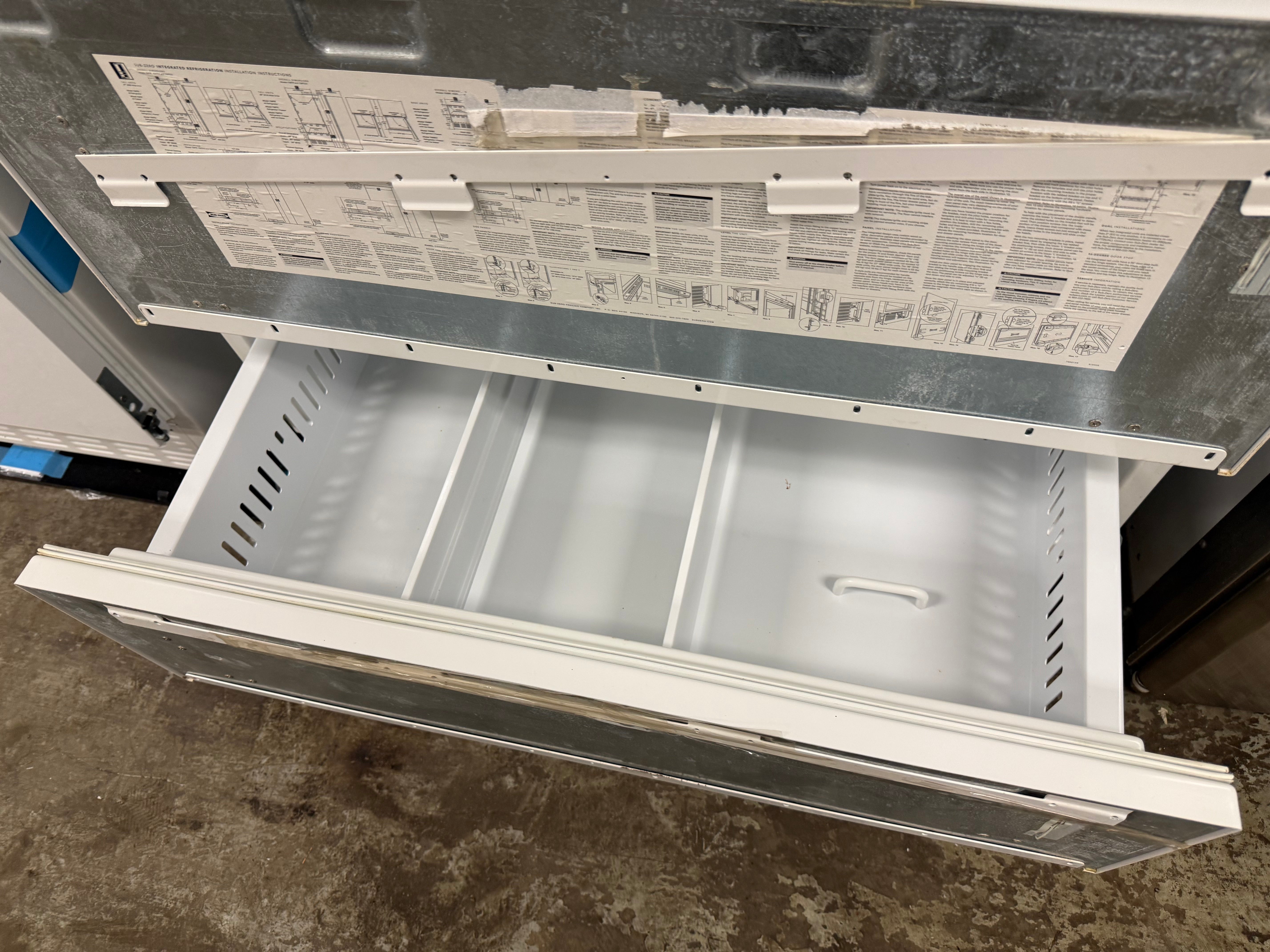A white drawer pull-out compartment of a metal appliance, shown partially extended with printed instruction labels visible on the inner panel.