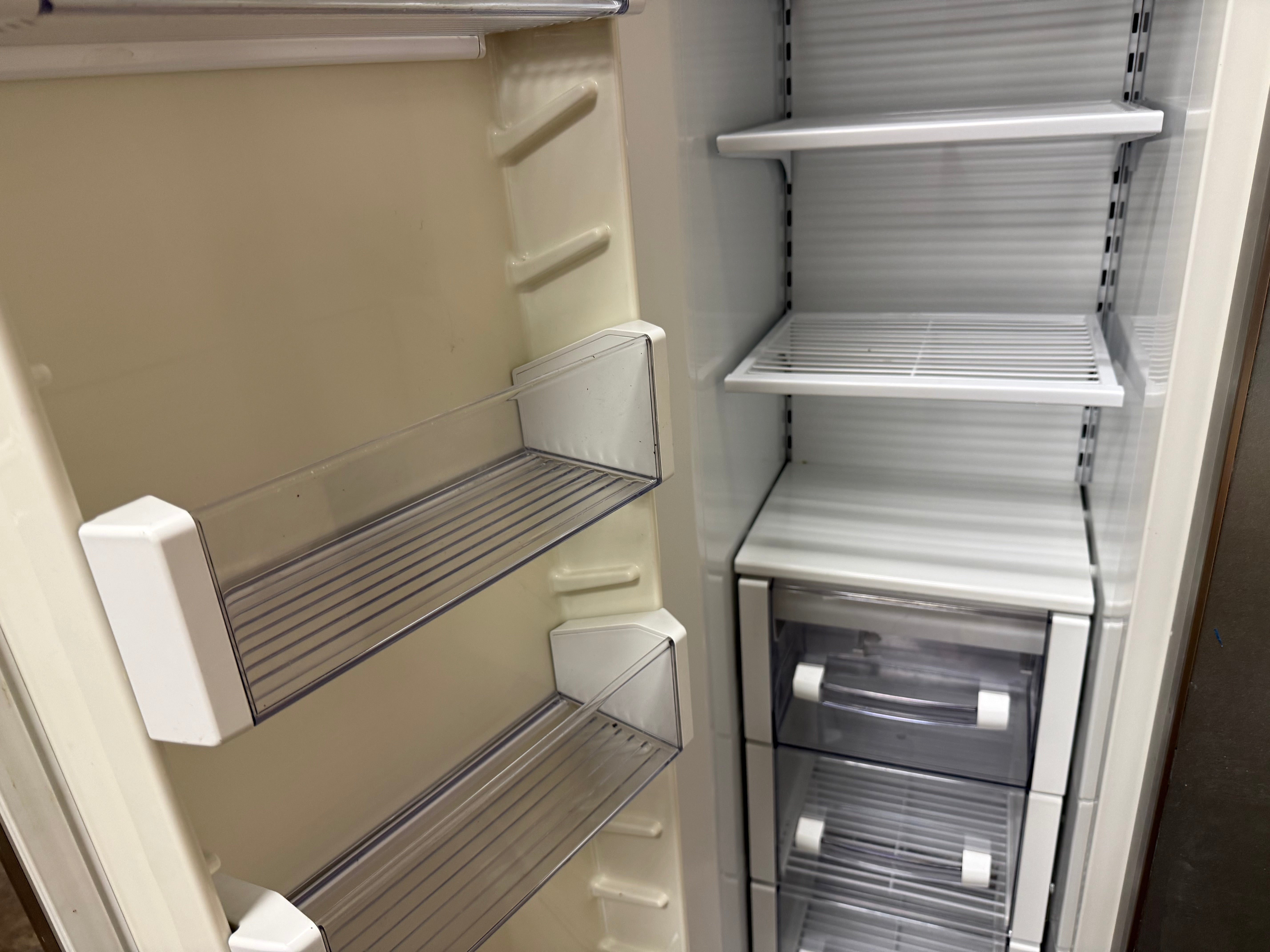An empty refrigerator interior with clear glass shelves, white door bins, and two lower transparent drawers on a light neutral background.