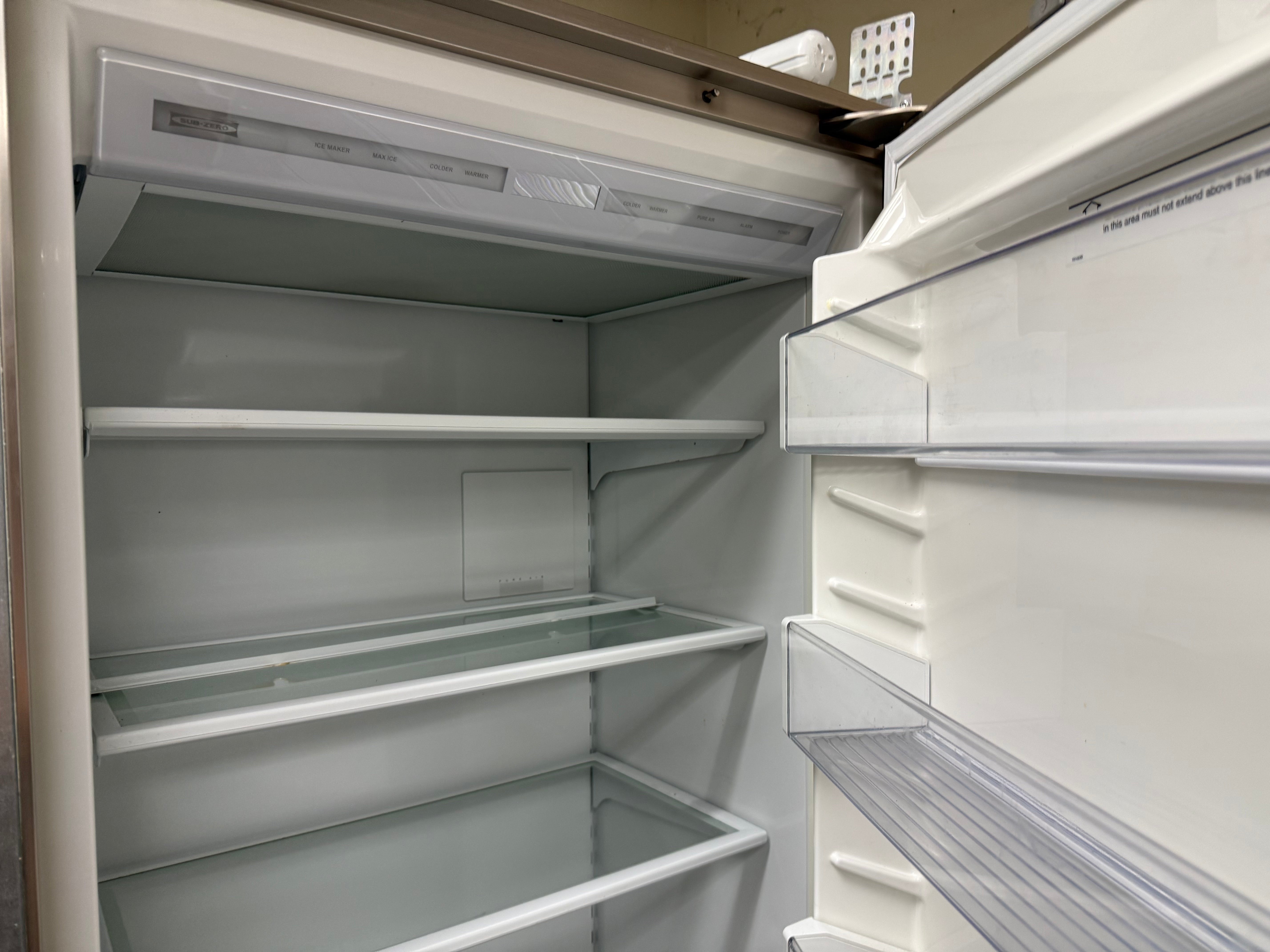An empty white refrigerator shown from the open door perspective, with interior shelves, glass trays, and door storage compartments visible.