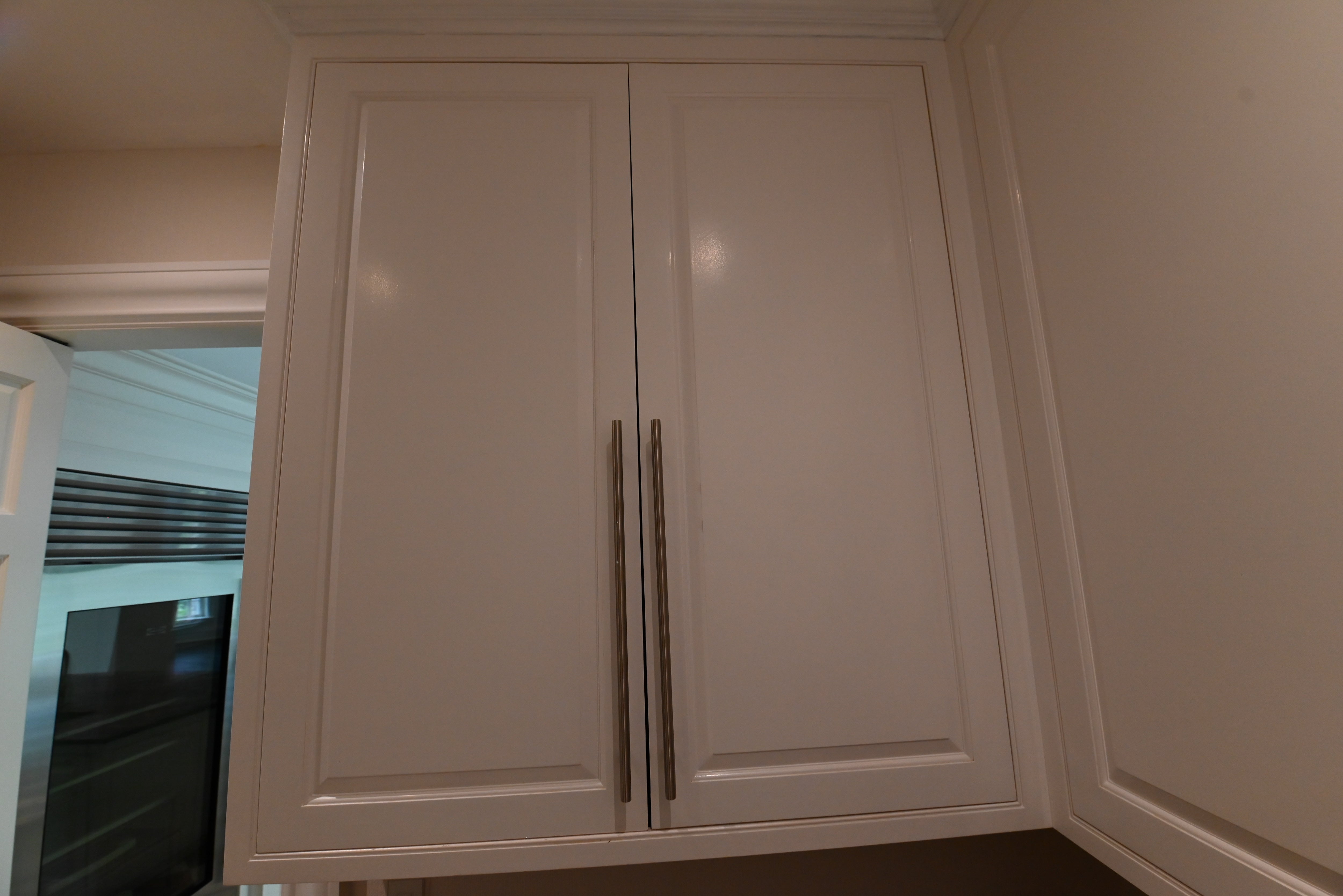 A pair of white shaker-style kitchen cabinets with long, slim vertical silver handles, set against a beige wall.