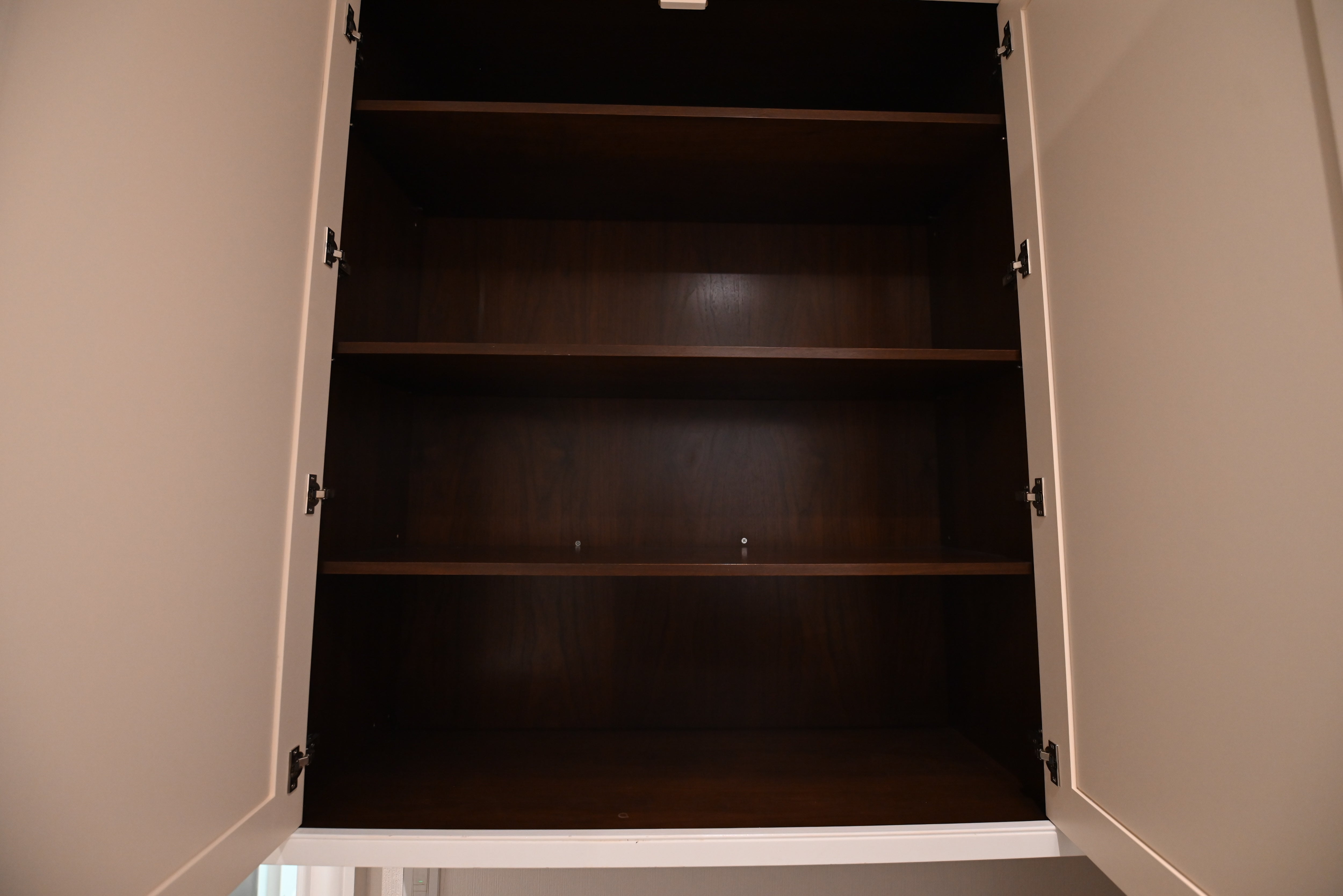 An open white cabinet with three dark brown wooden shelves, photographed from inside looking out.