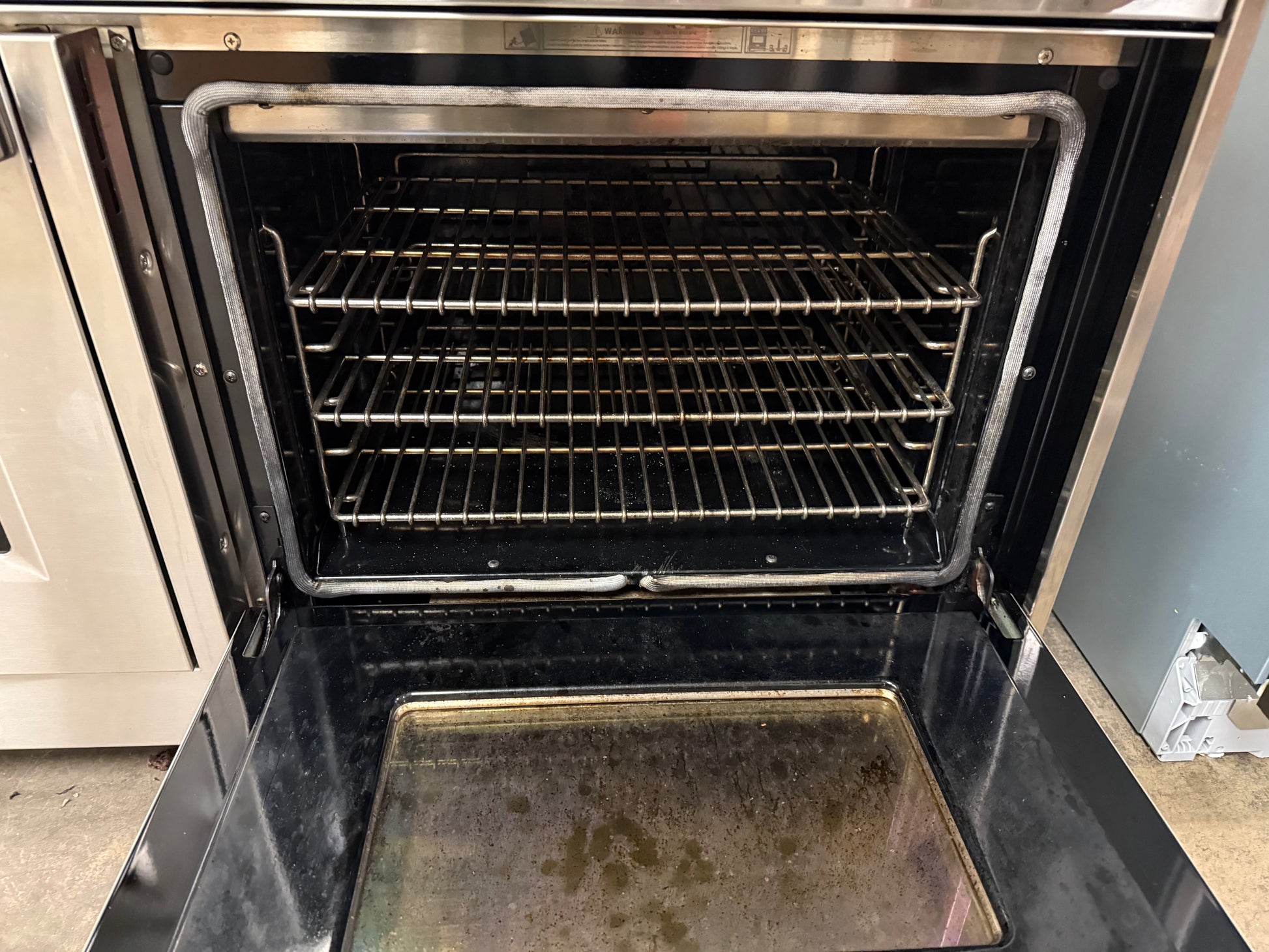 Oven with open door showing interior racks and a baking tray.