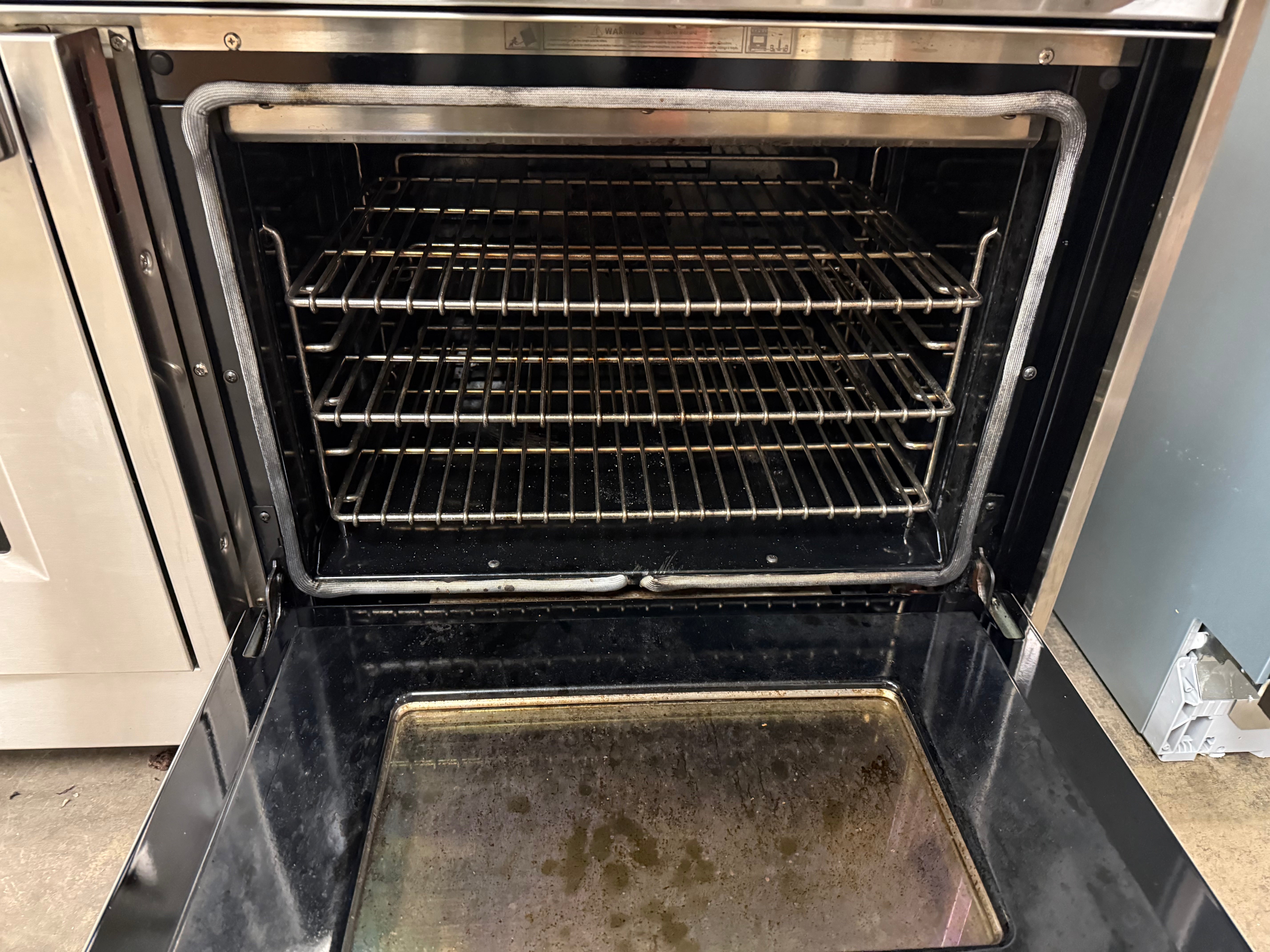 Oven with open door showing interior racks and a baking tray.