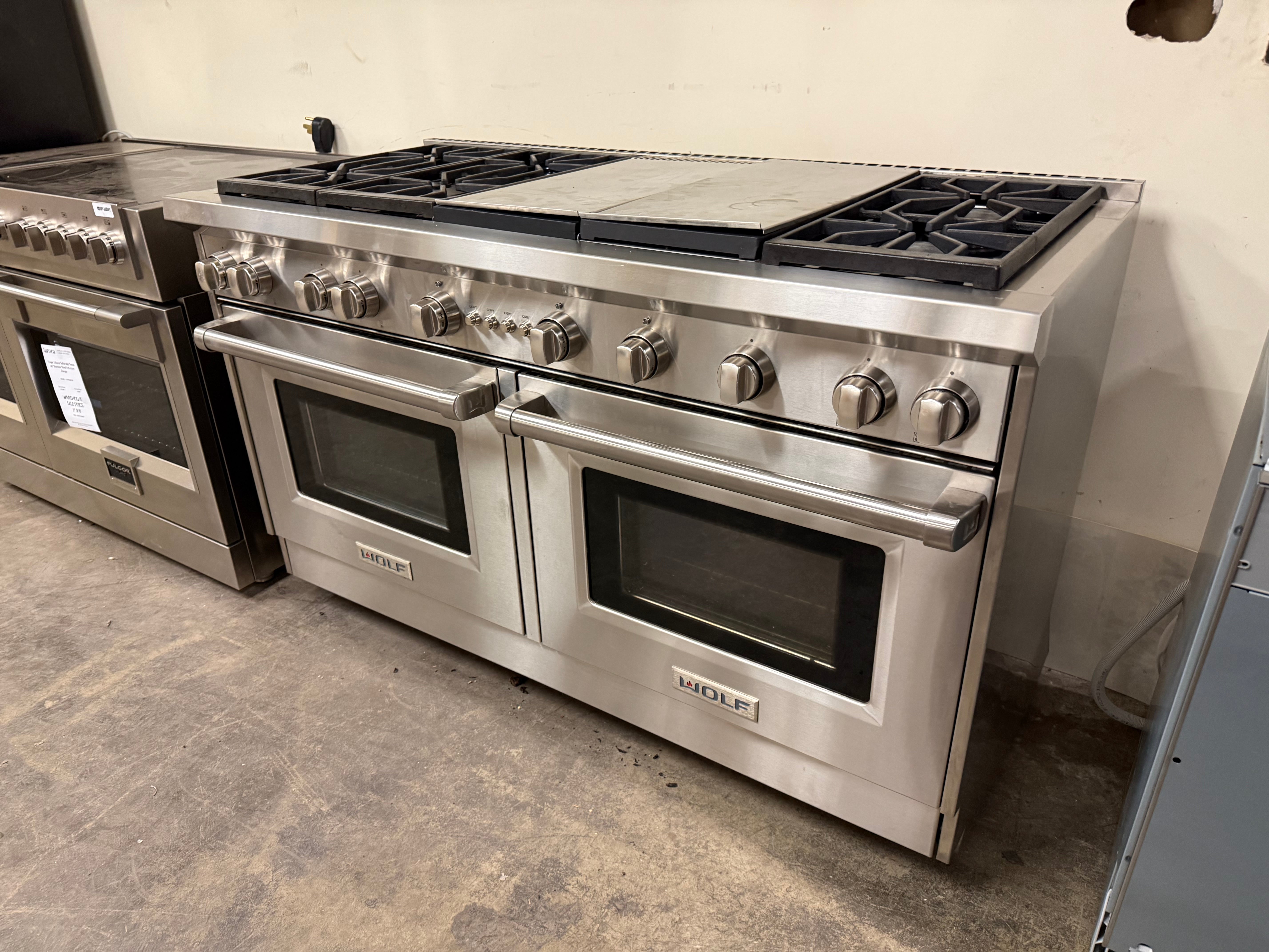 A Wolf 60-inch stainless steel range installed in a modern kitchen with marble backsplashes.