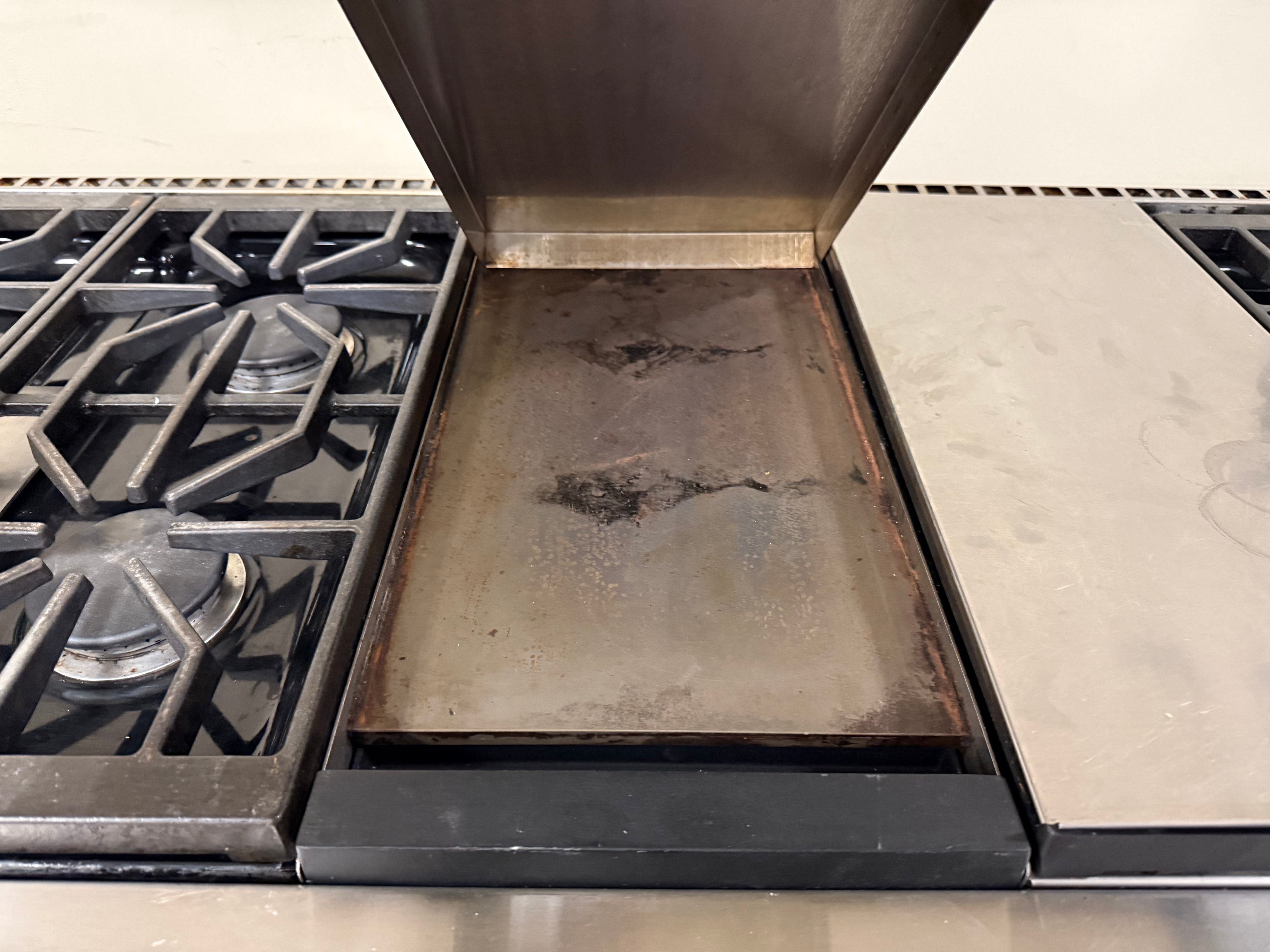 Top-down view of the built-in gas grill section located between the gas burners on the Wolf 60-inch range.