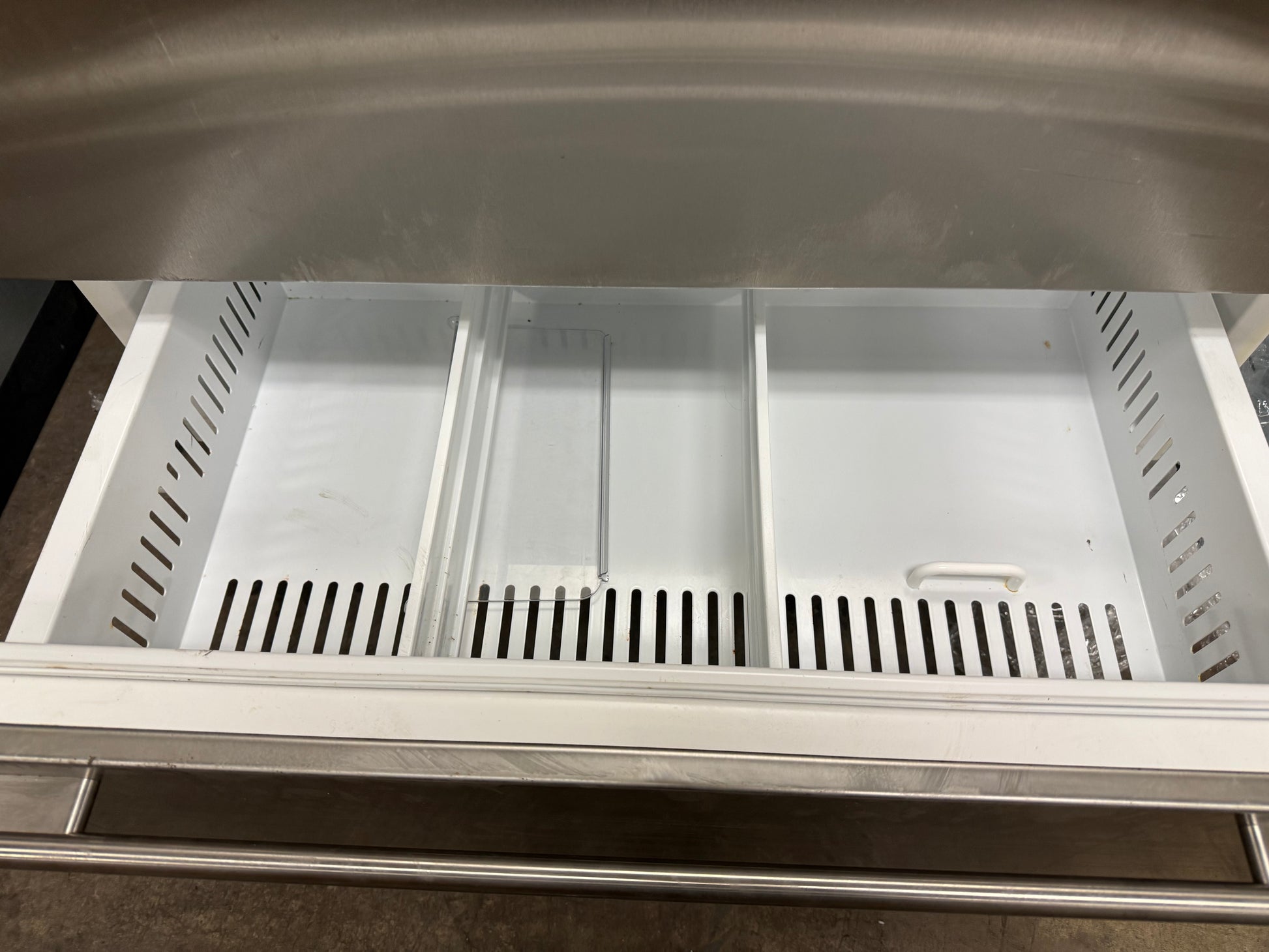 Stainless steel refrigerator drawer with cutout handles on a gray countertop