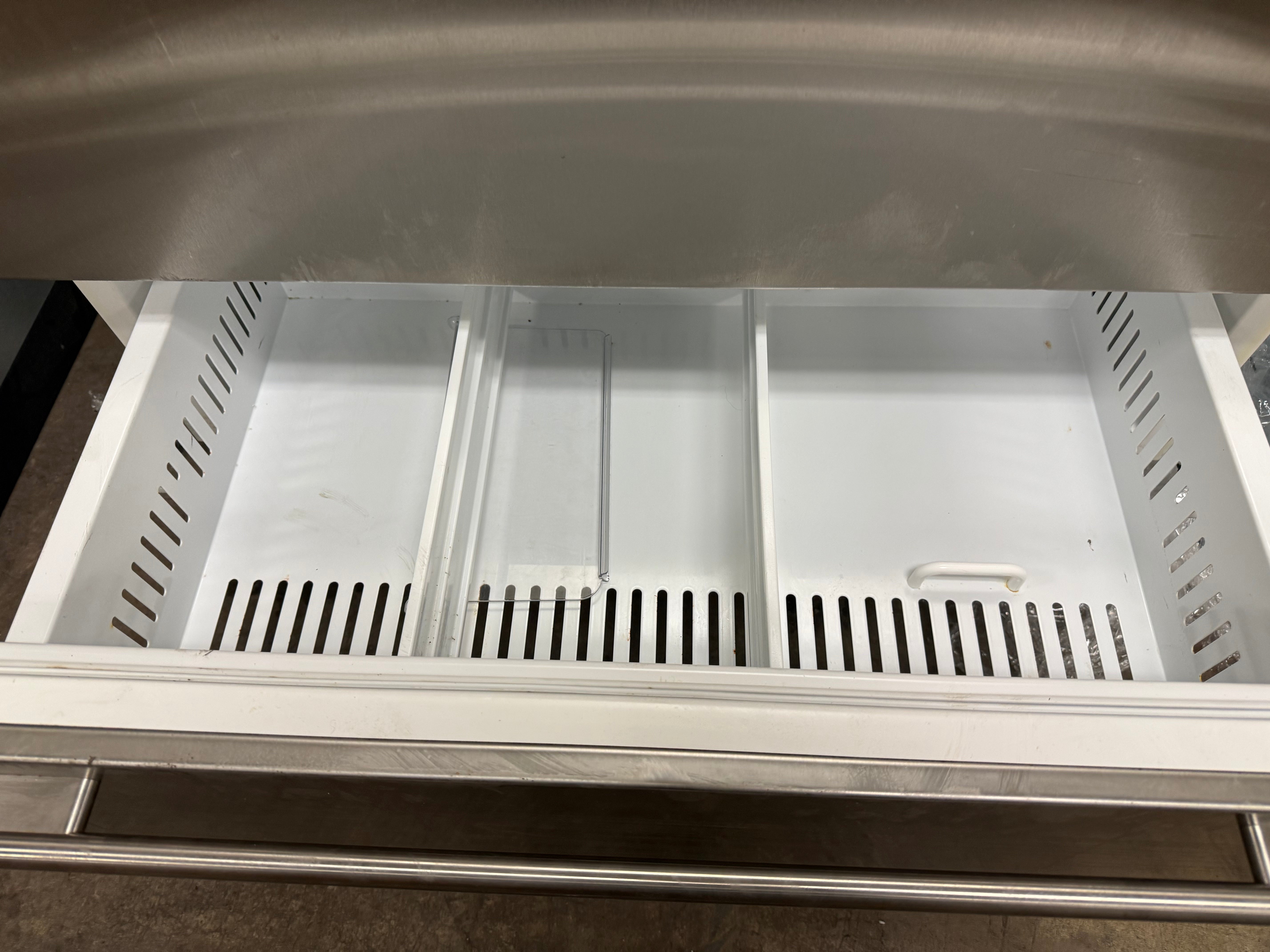 Stainless steel refrigerator drawer with cutout handles on a gray countertop