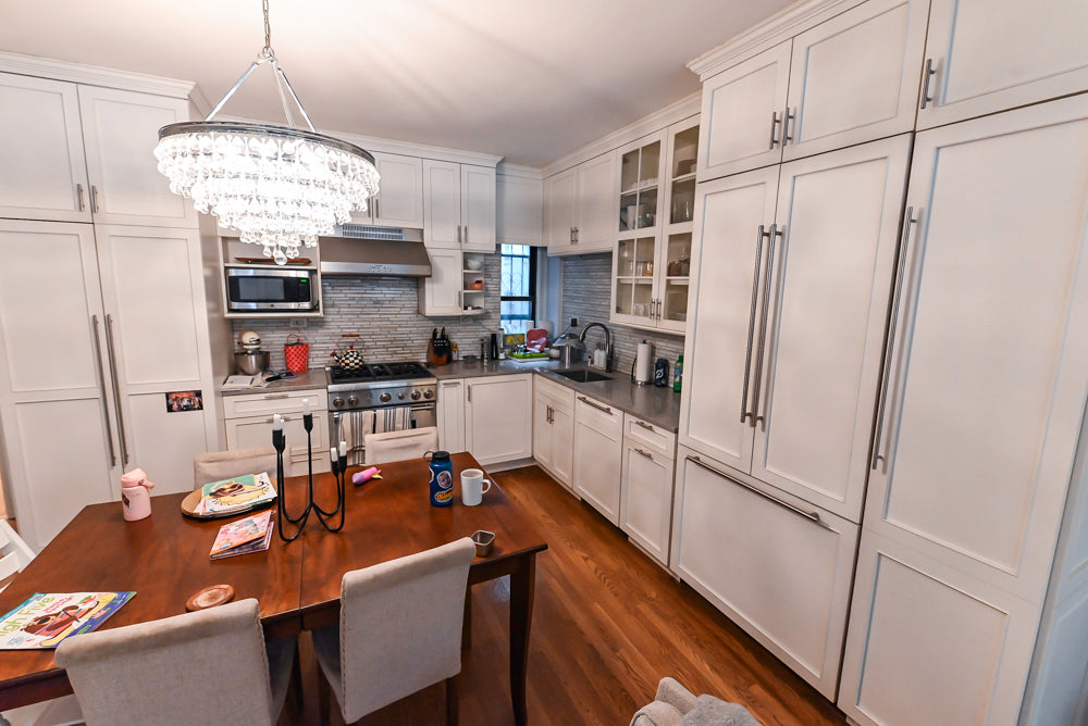 Modern kitchen with white cabinets, wooden dining table, and stainless steel appliances.