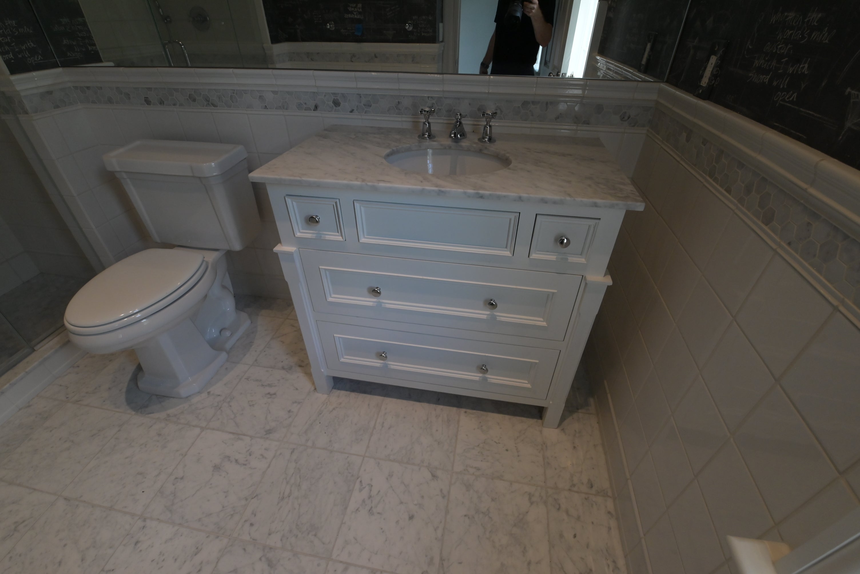 A light blue vanity cabinet with a white marble-look countertop and an undermount sink, shown in a tiled bathroom next to a white toilet.