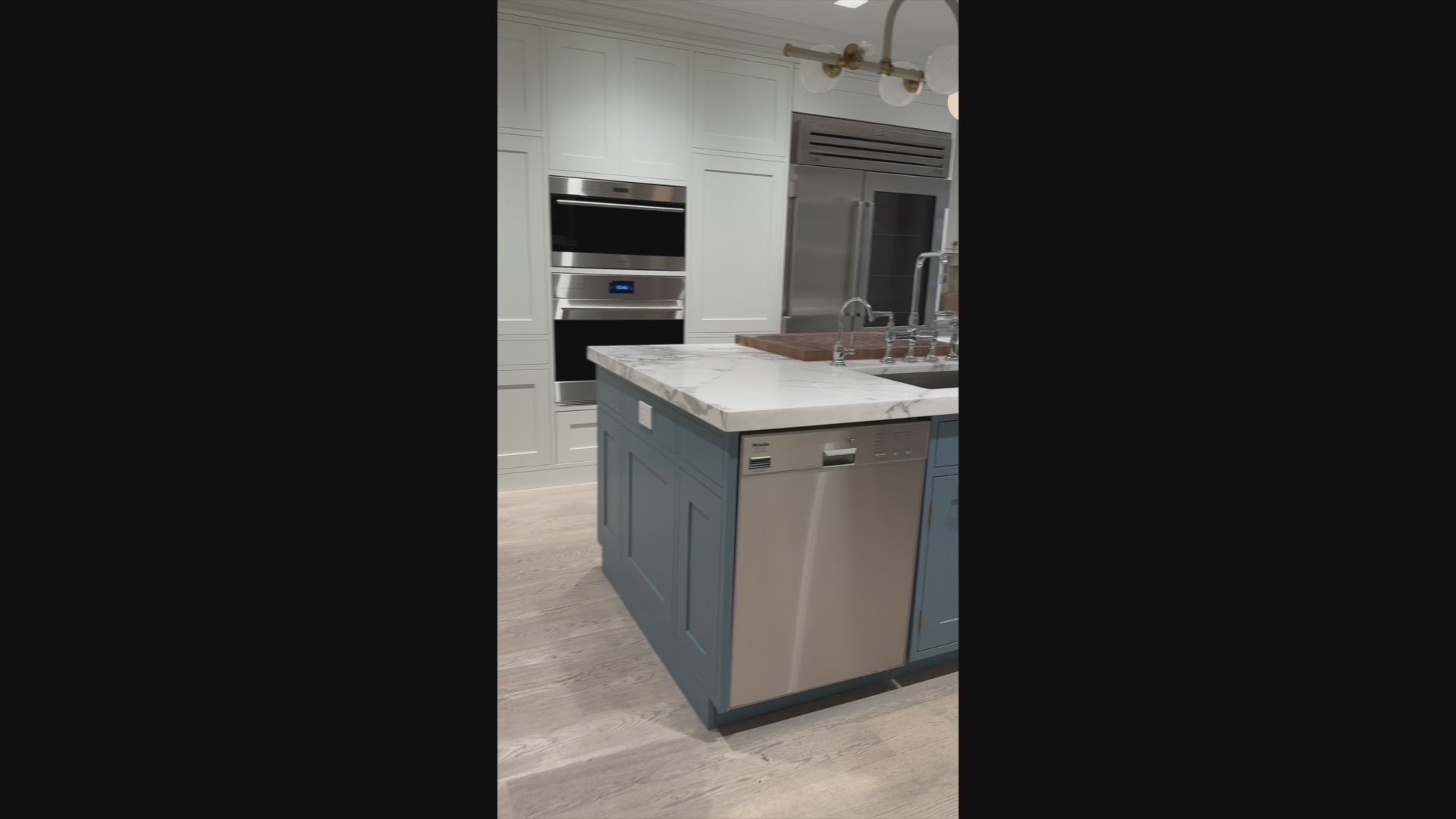 Load video: The Windermere transitional white custom kitchen featuring shaker cabinets, a quartz-topped island, and a Sub-Zero 648PROG glass door refrigerator